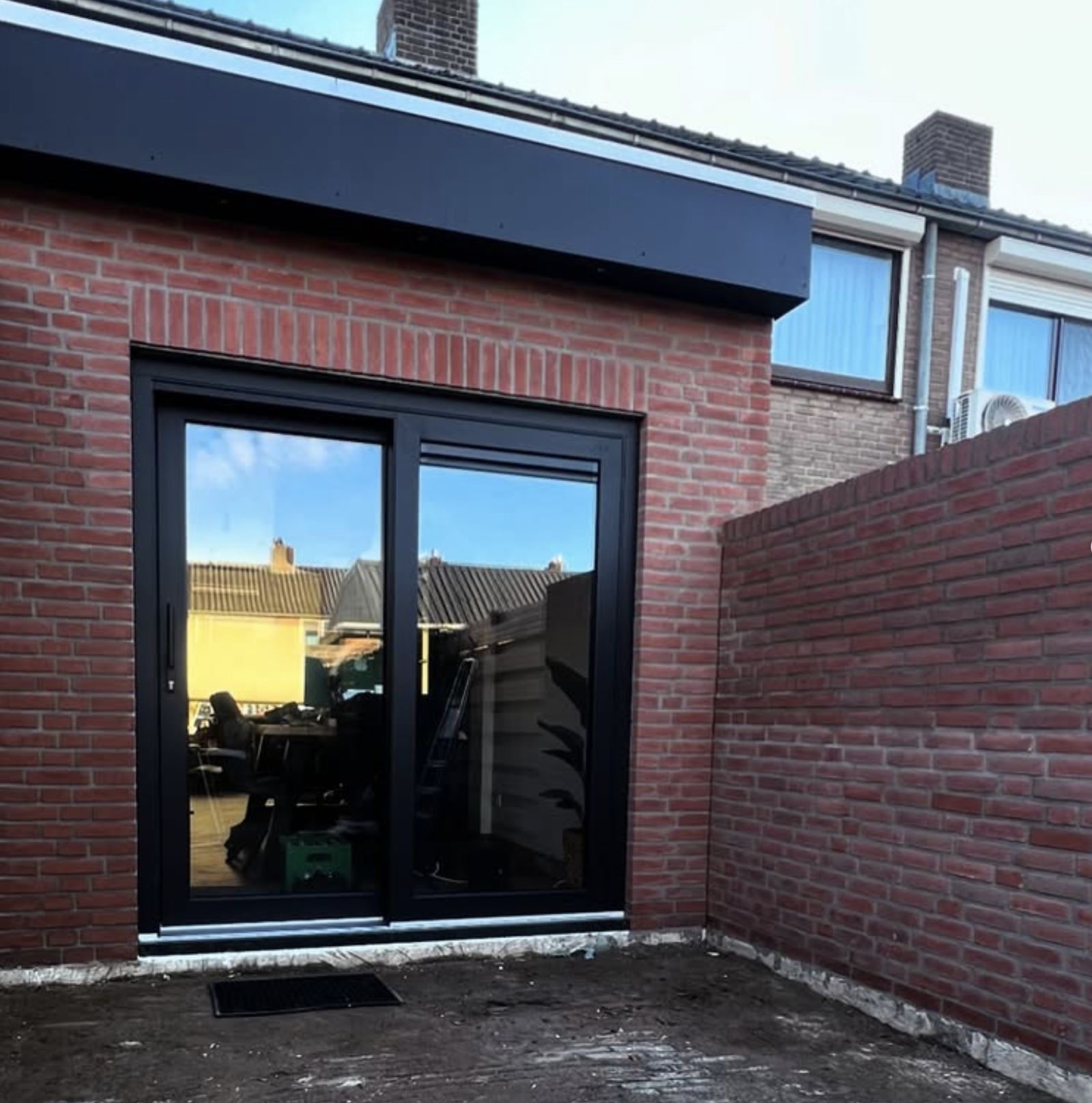 Aanbouw in metselwerk met zwarte schuifpui