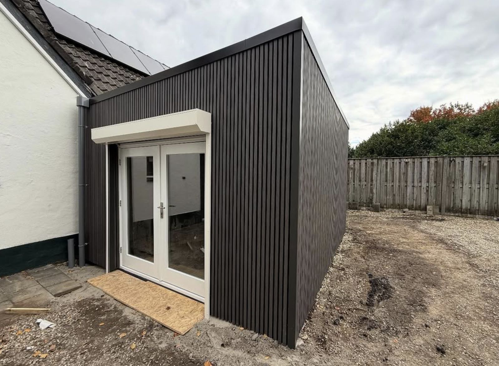 Moderne uitbouw met zwarte verticale gevelbekleding en openslaande deuren