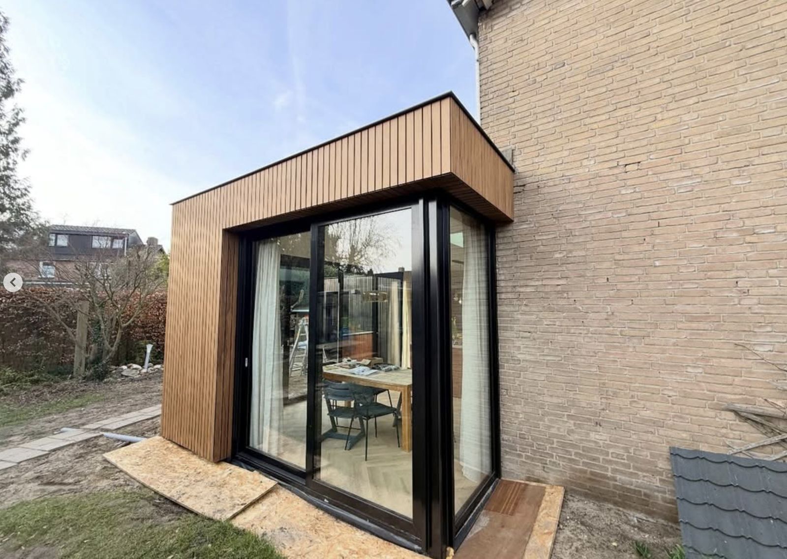 Detail van de houten gevelbekleding en zwarte kozijnen van de aanbouw