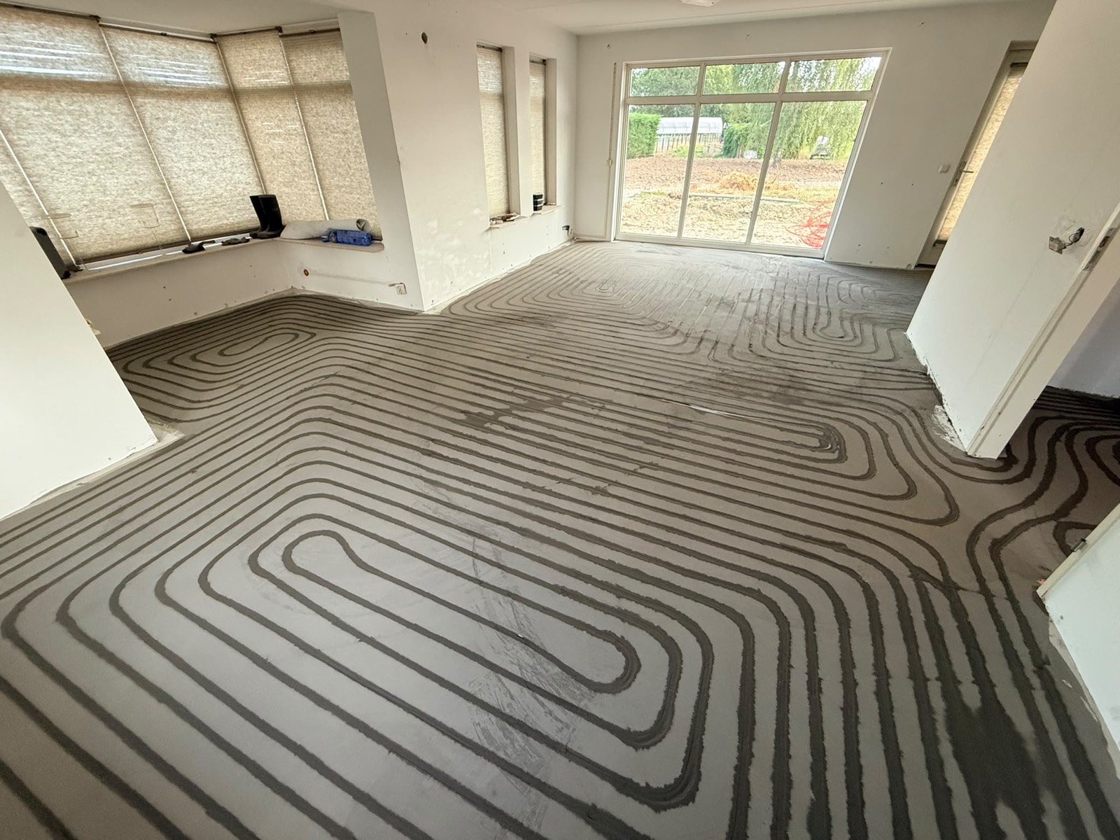 Woonkamer met aangelegde vloerverwarmingsleidingen en zicht op de tuin